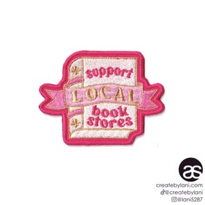May include: Pink embroidered iron-on patch with the text "Support Local Book Stores" in gold lettering. The patch features a stylized book with a pink ribbon.