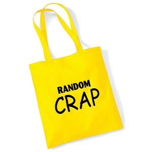 May include: Bright yellow tote bag with matching handles. The bag features the words "RANDOM CRAP" in bold, black capital letters. The bag is made of a sturdy material and is designed for carrying items.