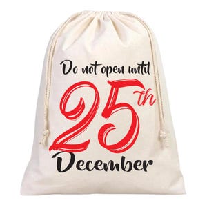 May include: A cream-coloured drawstring gift bag with the text "Do not open until 25th December" in black and red. The number 25 is in a large, bold, red font. The bag is made of a soft, natural fabric.