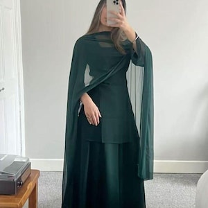 May include: A dark green ensemble featuring a long skirt, a top, and a sheer shawl. The outfit is a solid color, creating a sleek and elegant look. The shawl drapes over the shoulders, adding a touch of sophistication.