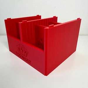Può includere: Una scatola rossa brillante per la conservazione di carte con divisori interni. La scatola presenta il testo "TCGVAULT" stampato sul davanti. Progettata per contenere carte collezionabili.