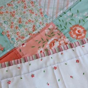 May include: Close-up of a patchwork quilt with various floral and patterned fabrics in shades of peach, teal, and white. The quilt features detailed stitching and a mix of small and large floral designs.