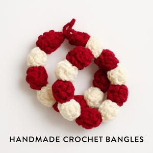 Könnte beinhalten: Handgefertigte Häkelarmbänder in runder Form. Die Armbänder wechseln sich zwischen Rot und Off-White ab und erzeugen ein Muster. Der Text "HANDMADE CROCHET BANGLES" wird unten im Bild angezeigt.