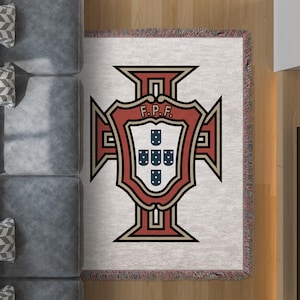 Può includere: Una coperta rettangolare con l'emblema della Federazione calcistica portoghese (FPF). L'emblema è uno scudo con un contorno rosso e nero, con le lettere "F.P.F." sopra uno scudo più piccolo contenente cinque scudi blu. La coperta ha un bordo sfrangiato.