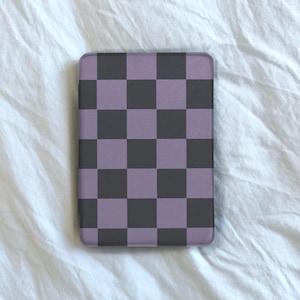 以下が含まれることがあります： 紫と黒の市松模様の長方形の携帯電話ケース。ケースは白いテクスチャのある表面に表示されています。