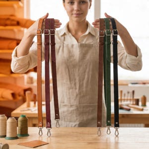 May include: A selection of leather straps in various colors, including brown, burgundy, green, and black. Each strap features silver-colored metal buckles and clasps. The straps are displayed against a neutral background, highlighting their craftsmanship.