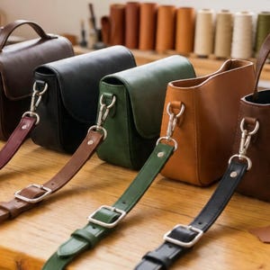 May include: A collection of leather crossbody bags in various colors, including brown, black, and green. Each bag features a flap closure, adjustable strap, and silver-tone hardware. The bags are displayed on a wooden surface.