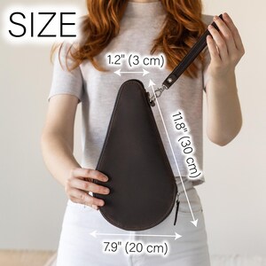 May include: A dark brown, teardrop-shaped clutch with a wrist strap. The clutch is 7.9 inches (20 cm) wide, 11.8 inches (30 cm) long, and 1.2 inches (3 cm) thick. It has a zipper closure and a silver-colored clasp.
