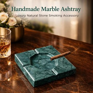 Può includere: Un posacenere quadrato in marmo verde scuro con finitura lucida e quattro poggia sigari integrati. Un sigaro marrone riposa nel bacino centrale. Il testo "Handmade Marble Ashtray" e "Luxury Natural Stone Smoking Accessory" è visibile.
