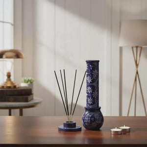 Peut inclure: Un ensemble de porte-encens bleu foncé avec un motif floral. L'ensemble comprend une base ronde avec des bâtonnets d'encens, un grand support cylindrique et un petit vase rond. Deux petites bougies chauffe-plat blanches sont également présentes.