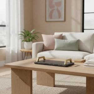 Peut inclure: Un plateau de service rectangulaire en marbre noir doté de deux poignées métalliques dorées sur les côtés courts. Le plateau présente une surface lisse et polie avec des veines grises naturelles, posé sur une table basse en bois clair.