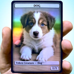 Può includere: Una carta collezionabile con un cucciolo con pelo marrone e bianco e occhi blu. La carta ha la parola "DOG" in alto, con il testo "Token Creature - Dog" e "1/1" in basso.