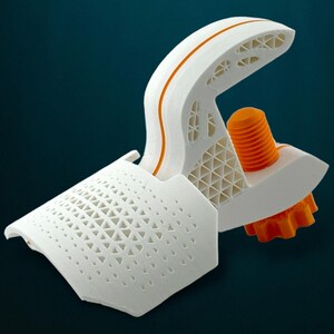 May include: A 3D-printed model with a white geometric design and orange highlights. It features a curved top with an orange stripe, a perforated panel, and an orange screw-like component. The background is a dark teal colour.