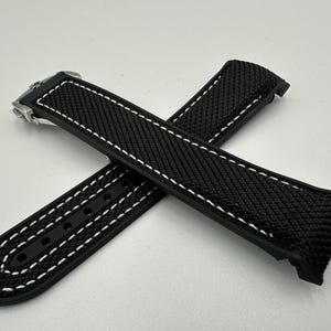 May include: Black watch strap with white stitching. The strap has a textured surface and a stainless steel buckle. The strap is designed to be durable and stylish, suitable for various watch styles.