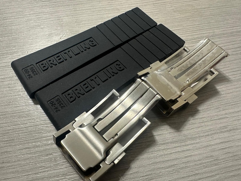 Puede incluir: Correas de reloj de goma negra con el nombre de la marca "Breitling" en relieve, junto con un cierre de reloj plateado. Las correas muestran la informaci&oacute;n de tama&ntilde;o "24-20 235S".