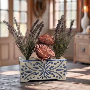 May include: A rectangular ceramic vase with a cream-colored base and blue floral patterns. It holds dried lavender and two peach-colored roses. The vase sits on a wooden table, creating a rustic, decorative display.