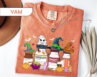 May include: An orange short-sleeve t-shirt featuring a graphic print of four medical vials wearing witch hats, labeled Midazolam, Diprivan, Fentanyl, and Ativan. The design includes a jack-o'-lantern, a purple cauldron, a small coffin, and a broom.