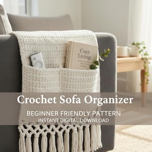 Op de afbeelding: Een crèmekleurige gehaakte sofa-organizer met zakken en franjes. De organizer bevat een afstandsbediening en een boek met de titel "Cozy Living". De tekst op de afbeelding luidt "Crochet Sofa Organizer" en "Beginner Friendly Pattern."