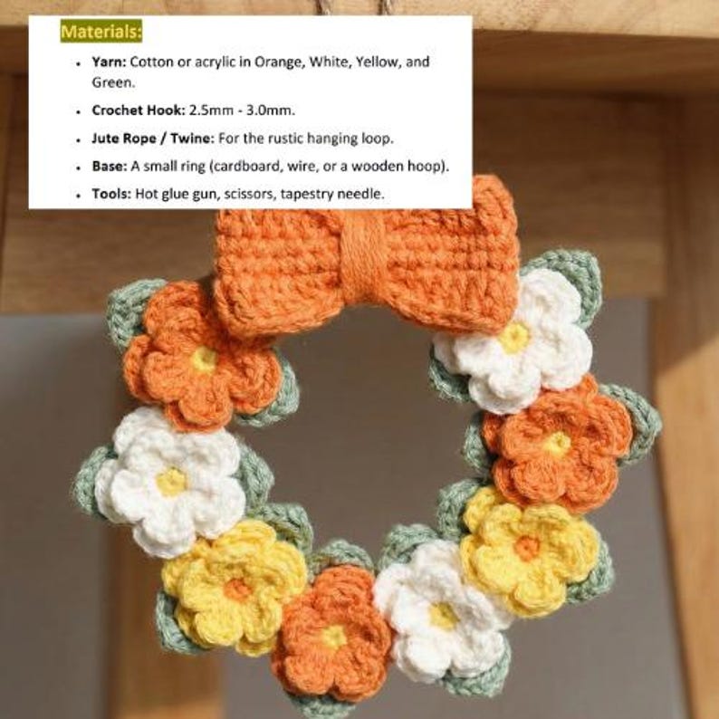 May include: A handmade crochet wreath featuring orange, white, and yellow flowers with green leaves. The wreath has an orange bow at the top. The materials include cotton or acrylic yarn, a crochet hook, jute rope, and a small ring base.