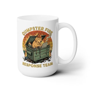 May include: White ceramic mug featuring a cartoon illustration of a golden retriever wearing a hard hat and working on a laptop inside a dumpster on fire. The text "DUMPSTER FIRE RESPONSE TEAM" is printed above and below the illustration.