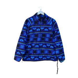May include: A blue fleece pullover with a geometric pattern in shades of blue, black, and green. The pullover has a half-zip closure and a drawstring at the bottom.