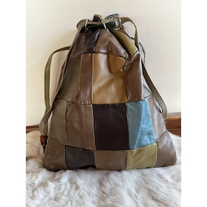 May include: A patchwork leather bucket bag with a drawstring closure and adjustable straps. The bag is made of different shades of brown, green, and blue leather.