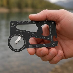 May include: A black multi-tool card held in a hand. The card features a key hole, ruler markings in inches and centimetres, and various wrench sizes. It also includes a bottle opener, can opener, and staple remover.