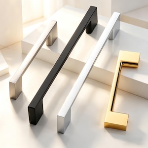 May include: Four cabinet pulls in different finishes: brushed silver, matte black, polished silver, and gold. Each pull has a rectangular bar design with square end caps. The pulls are arranged on a white surface.