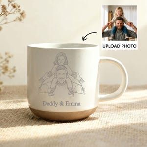 Pode incluir: Caneca de cerâmica creme com base castanha e alça grande. A caneca apresenta um desenho a traço de um pai carregando uma criança nos ombros, com o texto "Daddy & Emma" abaixo. Uma pequena foto é exibida com o texto "UPLOAD PHOTO".