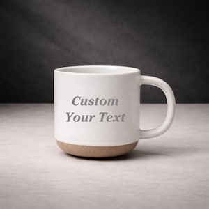 May include: White ceramic mug with a tan base and a curved handle. The mug features the text "Custom Your Text" in grey lettering. The mug is on a light-coloured surface.