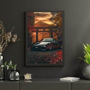 Peut inclure: Impression d'art encadrée représentant une voiture de sport noire sur une route bordée de feuilles rouges, devant un portail torii japonais, une montagne et un feuillage d'automne. L'œuvre est affichée sur un mur gris foncé.