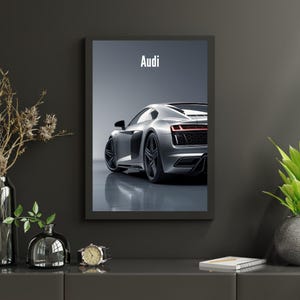 May include: Framed print featuring a silver Audi sports car, viewed from the rear. The car is positioned on a reflective surface, with the word "Audi" in white at the top. The image is set against a gray backdrop.