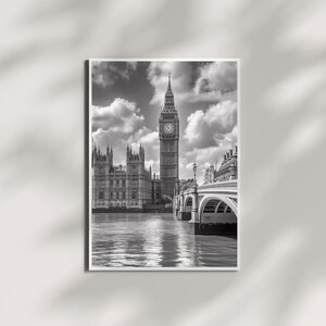 May include: Black and white framed print of the Palace of Westminster and Elizabeth Tower, also known as Big Ben, in London. The image captures the iconic architecture, the Thames River, and a cloudy sky.