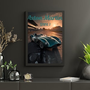 May include: Framed print featuring a teal Aston Martin DBR1 race car on a racetrack. The image has the text "Aston Martin DBR1" in teal script. The background shows a sunset over the track.