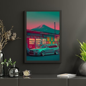 May include: Framed art print featuring a teal station wagon parked in front of a vending machine and a mountain. The sky transitions from teal to pink. The car has a lowered suspension and custom wheels. The print is in a black frame.