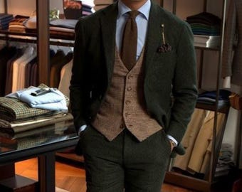 May include: A dark green three-piece suit with a brown waistcoat, light blue shirt, and brown tie. The suit is worn with brown leather shoes. The background shows a clothing store with racks of clothing.