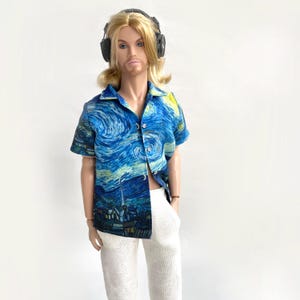 Puede incluir: Una muñeca con una camisa de manga corta con un estampado de la pintura "La noche estrellada" de Van Gogh. La camisa se combina con pantalones blancos. La muñeca también tiene auriculares.
