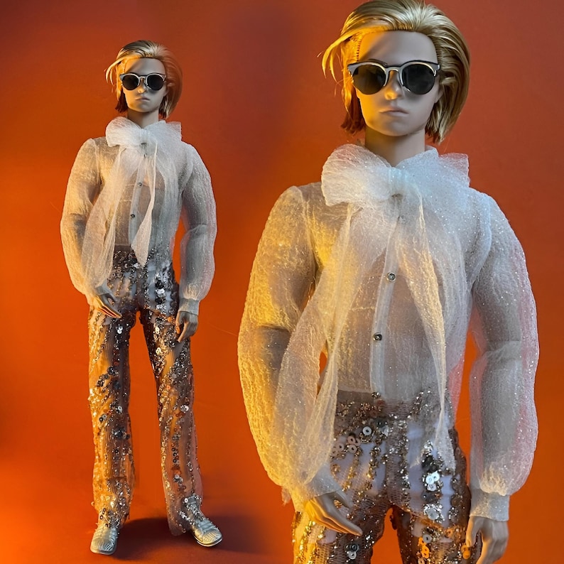 May include: A doll wearing a sheer white blouse with a large bow, sunglasses, and sequined pants. The doll has blonde hair and silver shoes. The background is a solid orange color. The doll is posed in front of a matching doll.