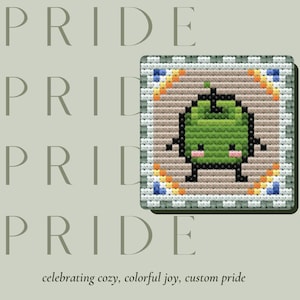 Puede incluir: Diseño cuadrado de punto de cruz con un personaje verde de dibujos animados con extremidades negras y una cara sonriente. El diseño está sobre un fondo beige con un borde colorido. La palabra "PRIDE" está apilada verticalmente a la izquierda, con la frase "celebrating cozy, colorful joy, custom pride" en la parte inferior.