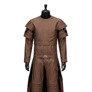 May include: A brown costume comprising a long coat, trousers, and a top with shoulder detailing. The costume features a futuristic design with stitched elements and a belt. The trousers have knee padding and a pocket. The costume is displayed on a black mannequin.