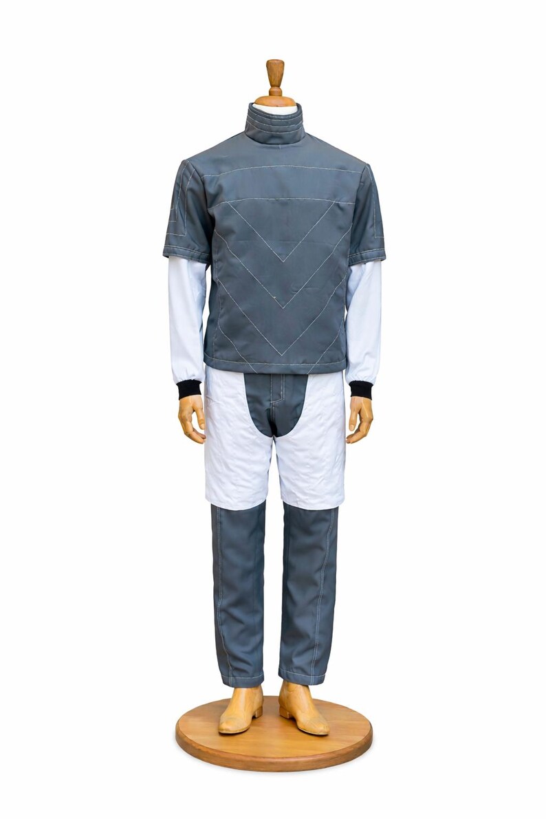 May include: A gray and white outfit displayed on a mannequin. The outfit includes a short-sleeved gray jacket with white stitching, a white long-sleeved undershirt, white shorts, and gray pants. The mannequin is on a wooden base.