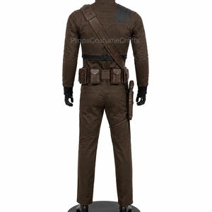 May include: A brown long-sleeved jumpsuit featuring a textured fabric, a black collar, and black cuffs. The outfit includes a brown utility belt with multiple pouches, a diagonal shoulder strap, and a holster attached to the left thigh area.
