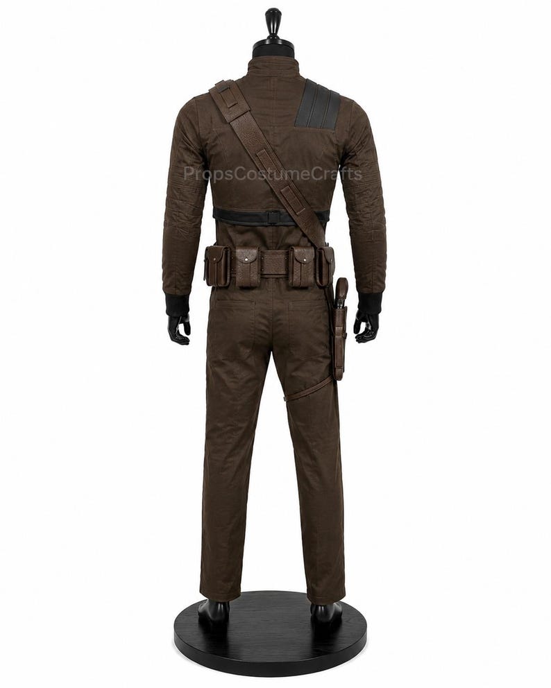 May include: A brown long-sleeved jumpsuit featuring a textured fabric, a black collar, and black cuffs. The outfit includes a brown utility belt with multiple pouches, a diagonal shoulder strap, and a holster attached to the left thigh area.