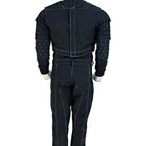 May include: Black jumpsuit with white stitching details. The suit features a high collar, shoulder accents, and geometric patterns on the sleeves. The pants have a straight leg design. The suit is displayed on a mannequin.