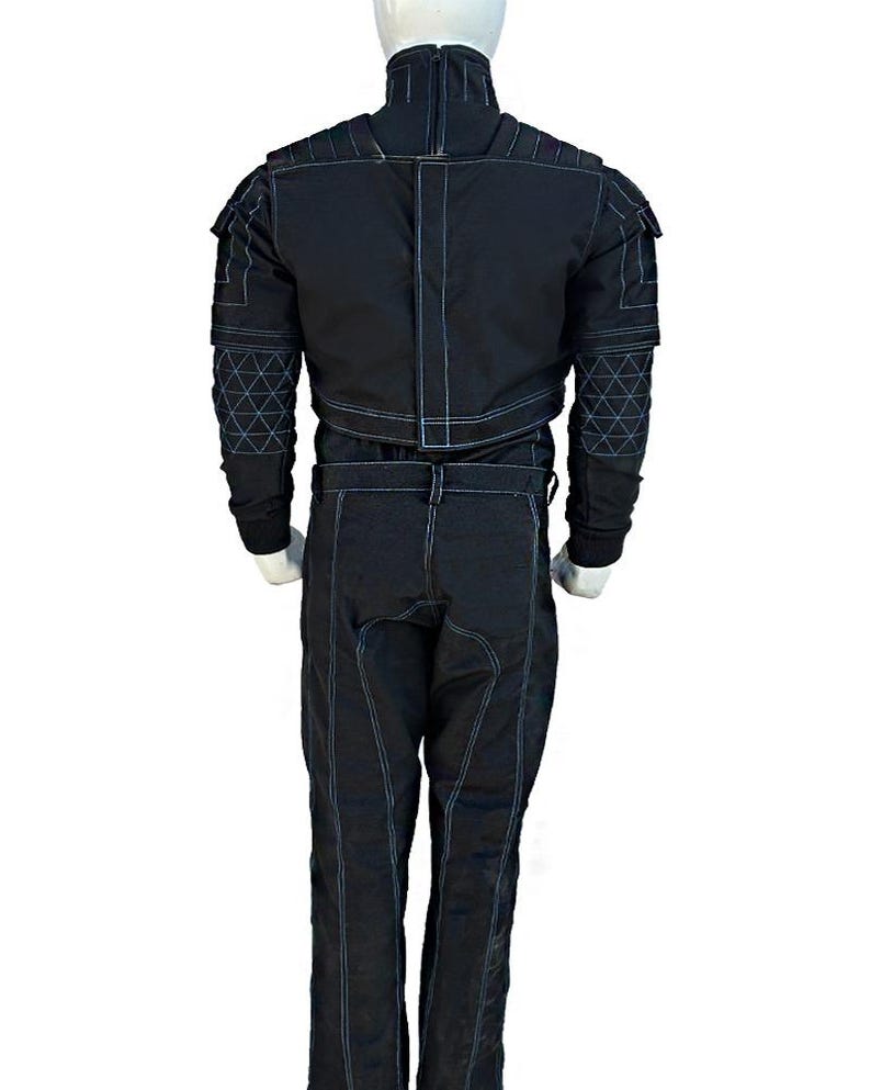 May include: Black jumpsuit with white stitching details. The suit features a high collar, shoulder accents, and geometric patterns on the sleeves. The pants have a straight leg design. The suit is displayed on a mannequin.