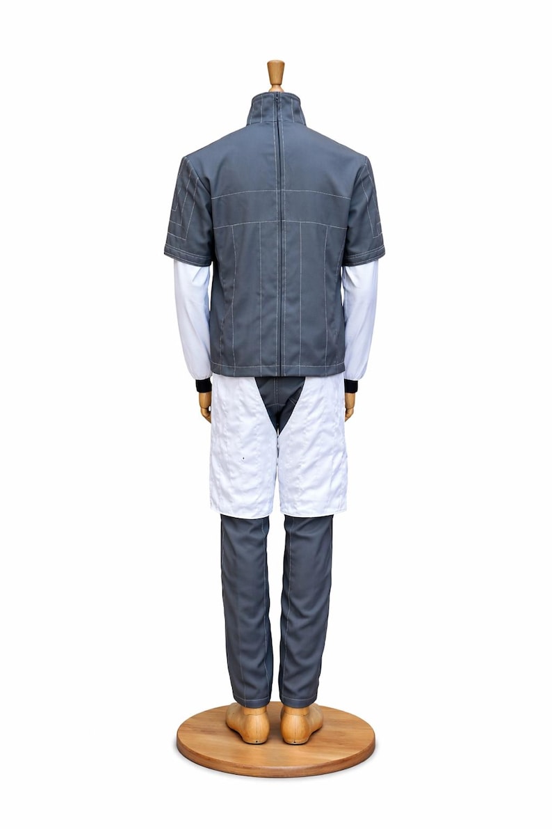 May include: A gray and white uniform displayed on a mannequin. The outfit includes a short-sleeved gray jacket with white stitching, a white long-sleeved shirt, gray pants, and white shorts. The mannequin stands on a wooden base.