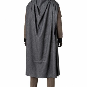 May include: A long, dark grey hooded cloak worn over a brown jacket with black cuffs, brown trousers, and black boots. The cloak features a textured fabric and drapes down the back. The text PropsCostumeCrafts is visible on the lower cloak.