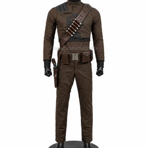 May include: A brown long-sleeved shirt and matching trousers costume set on a mannequin. The outfit includes a dark brown diagonal shoulder strap with silver-toned cylindrical accents, a utility belt with pouches, and a holster for a sidearm.