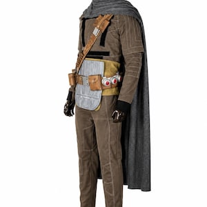 May include: A brown long-sleeved jumpsuit with white stitching, a grey cape, and a tan utility belt featuring silver plates, brown pouches, and three circular red accents. The outfit includes black gloves and black boots on a dark mannequin.