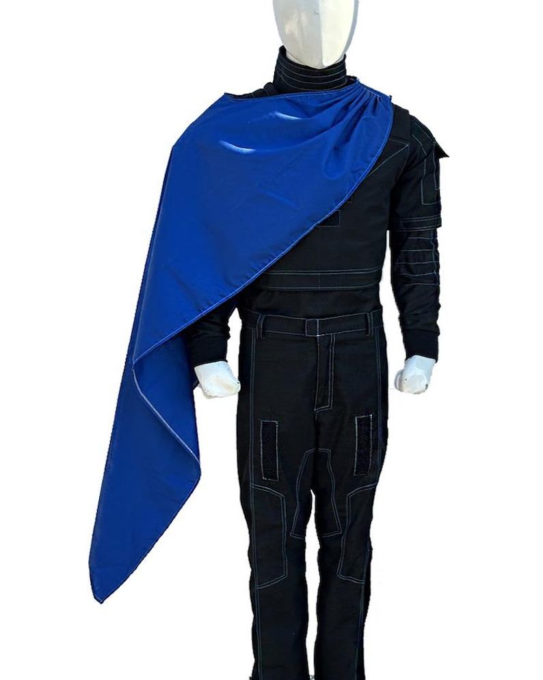 May include: A black jumpsuit with white stitching and a high collar, paired with a vibrant blue cape. The cape is draped over the shoulder, creating a striking contrast against the dark attire. The outfit is displayed on a mannequin.